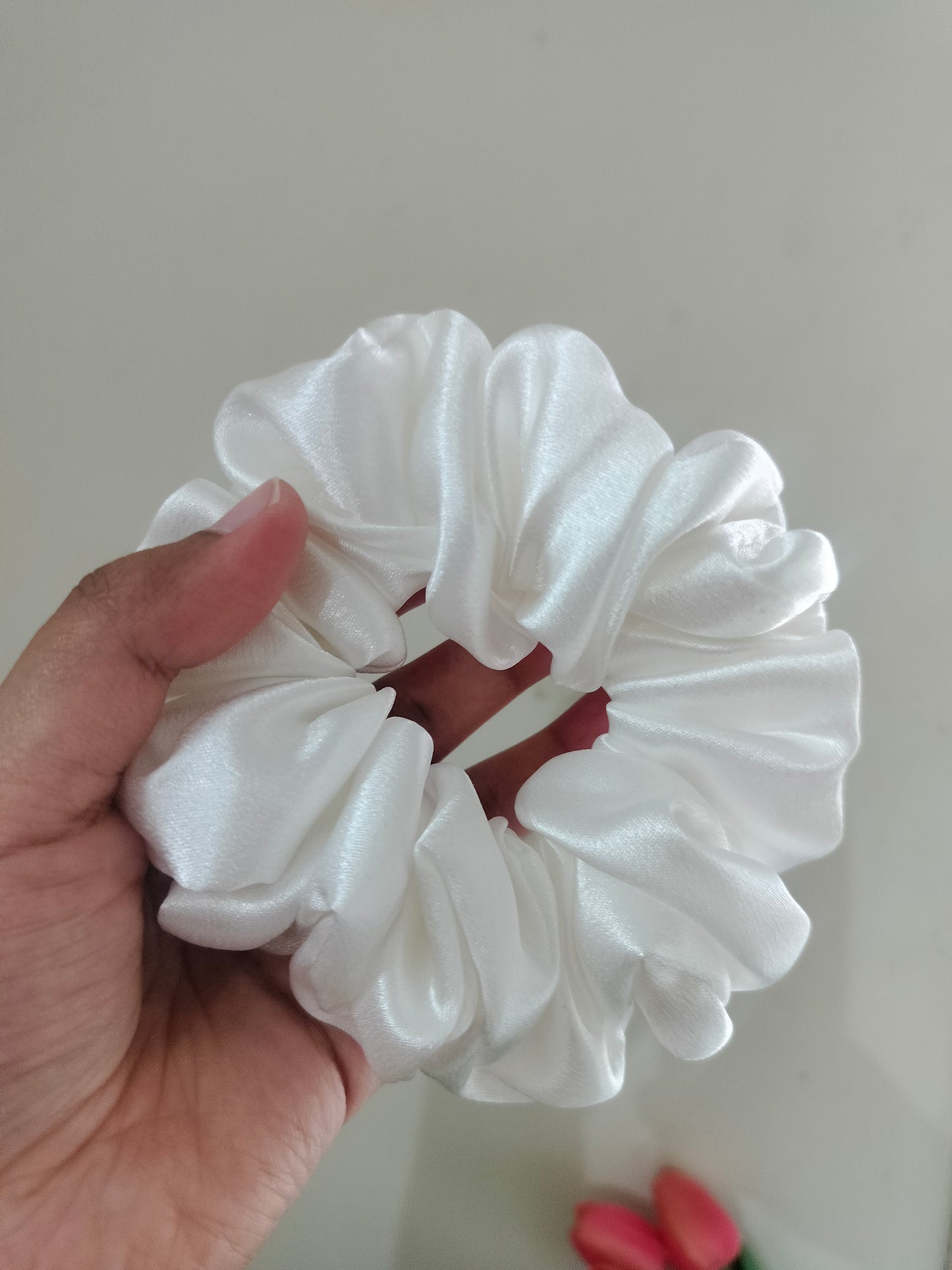 White silk scrunchie held in a hand against a plain background