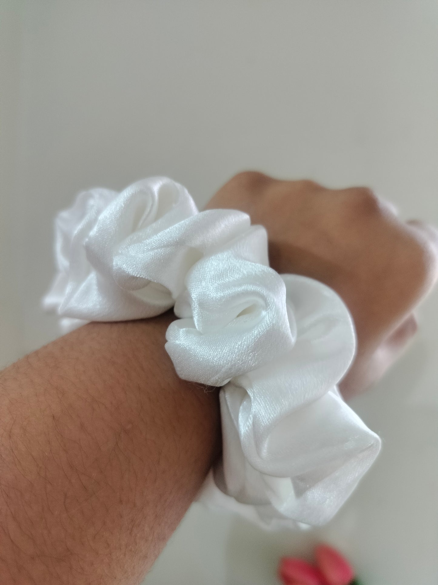 White silk scrunchie on a wrist with a neutral background